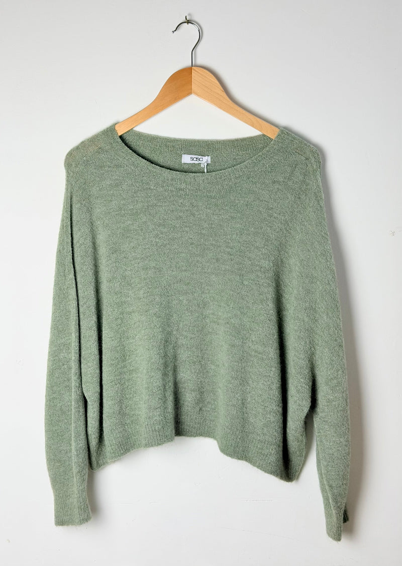 Green sweater on a wooden hanger against a white background