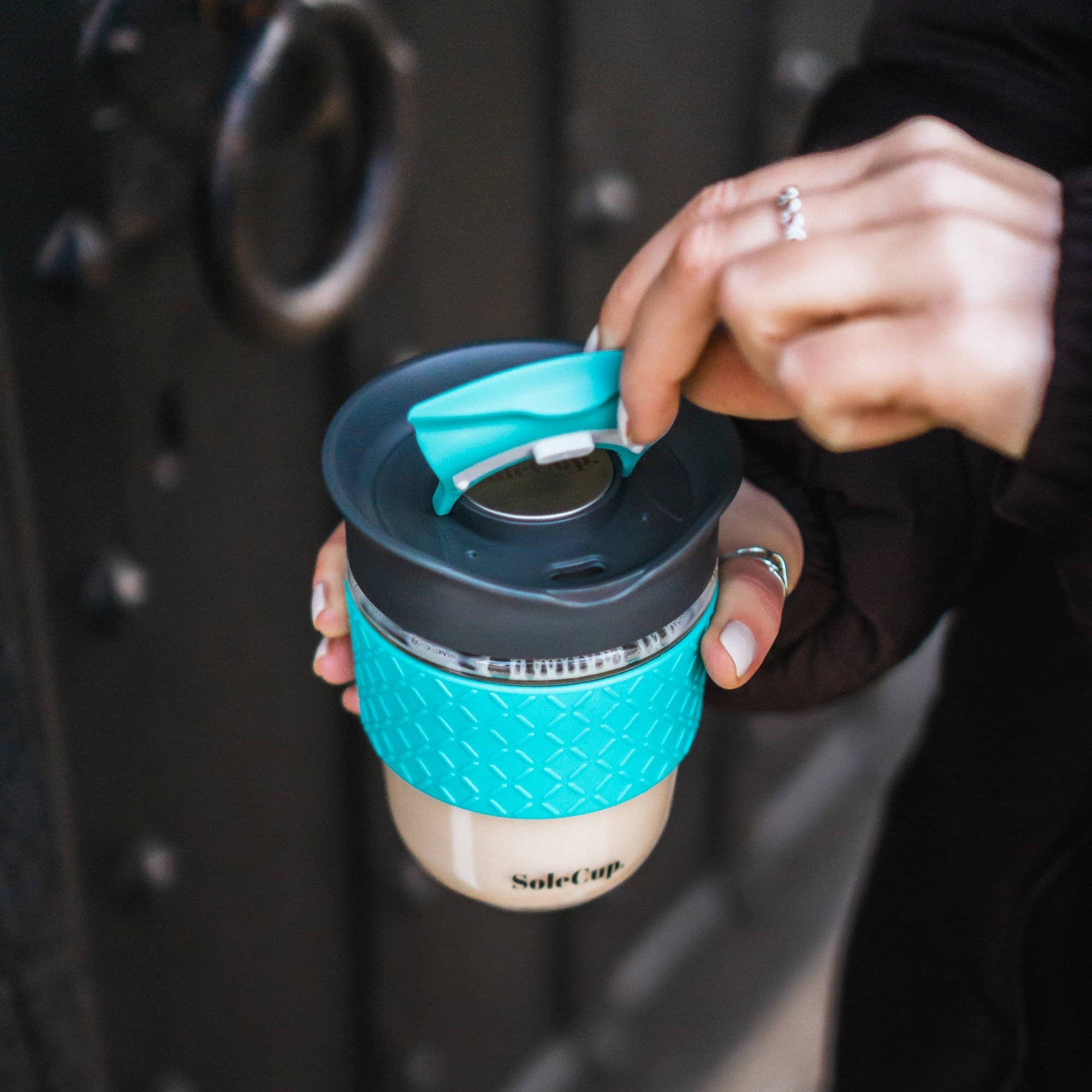Person holding a blue and black reusable coffee cup with a textured sleeve.