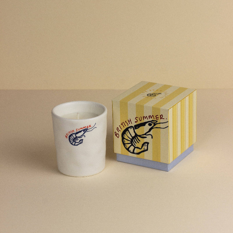 Candle with 'British Summer' design next to its packaging on a beige background