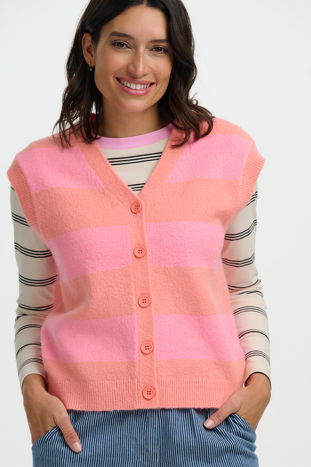 Woman wearing a Sugarhill Amber pink and peach striped cardigan over a striped shirt on a white background