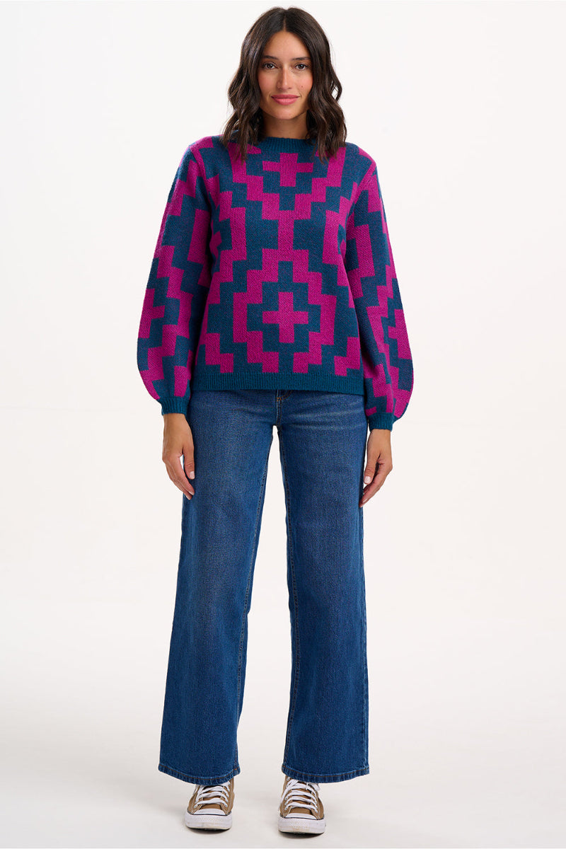 Woman wearing a Sugarhill Essie Jumper Teal/Pink Diamond and jeans on a white background