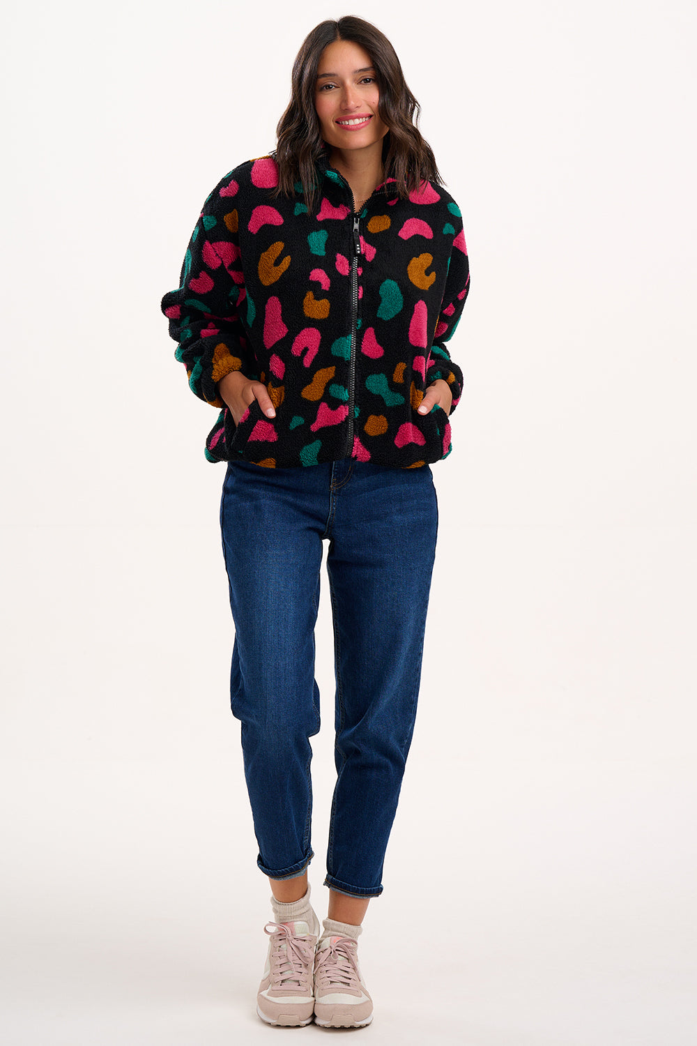 Woman wearing a colorful patterned jacket and blue jeans on a white background