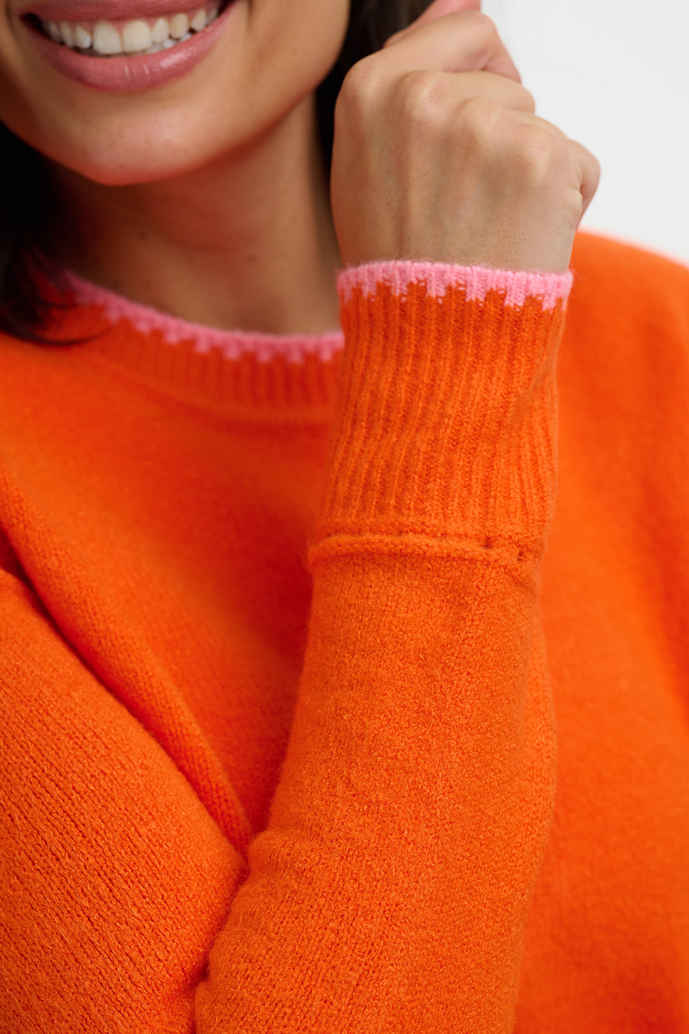 Close-up of a person wearing an orange sweater with pink trim on the cuffs.