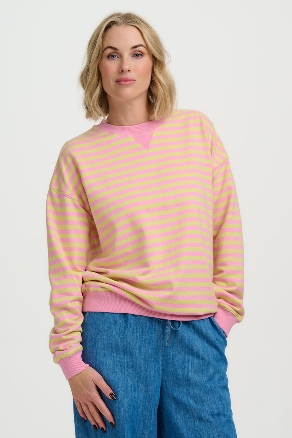 Woman wearing a Sugarhill Lucia Sweatshirt-Pink/Yellow with blue jeans on a white background