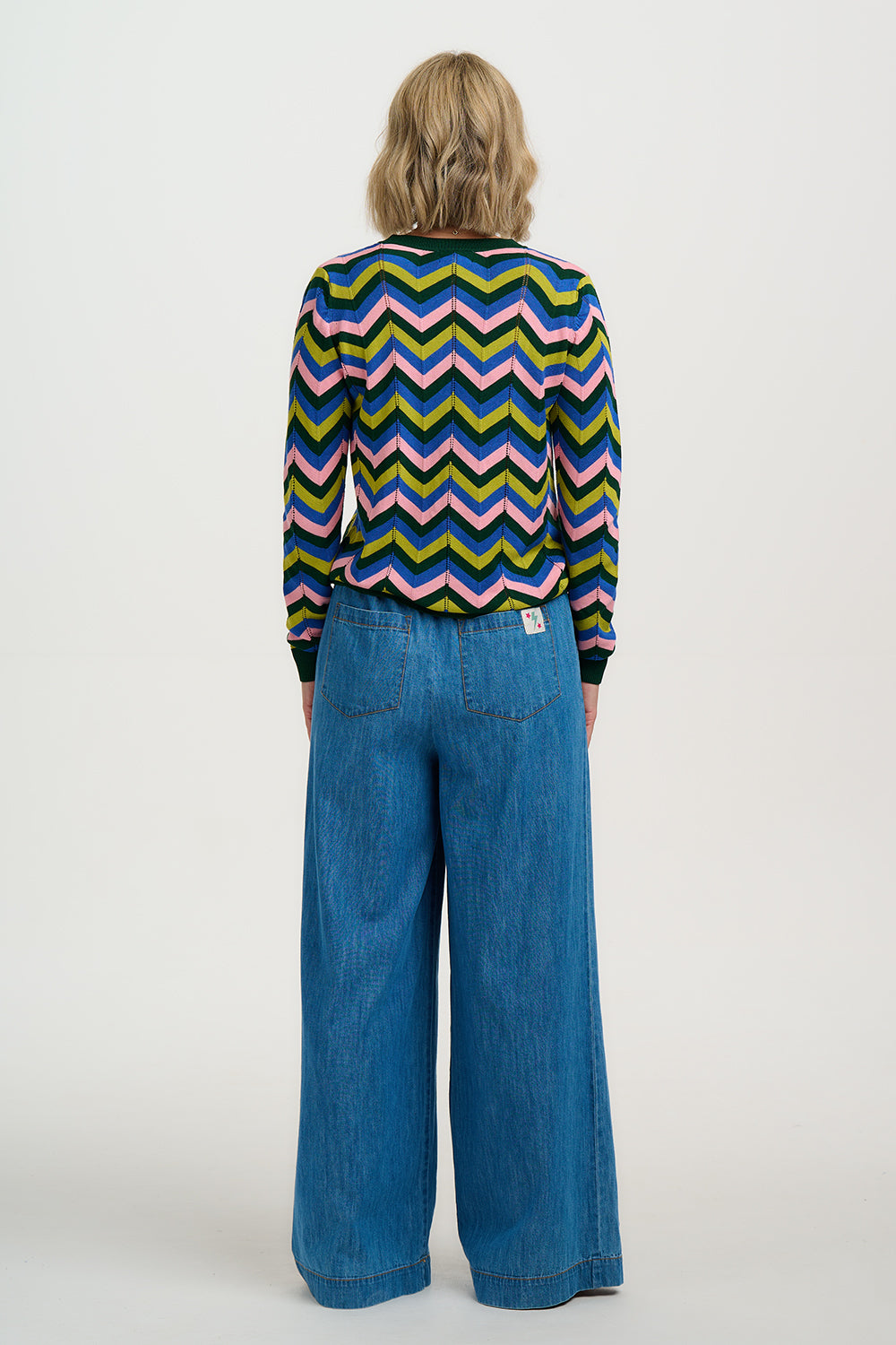 Person wearing a colorful zigzag patterned shirt and blue jeans on a white background