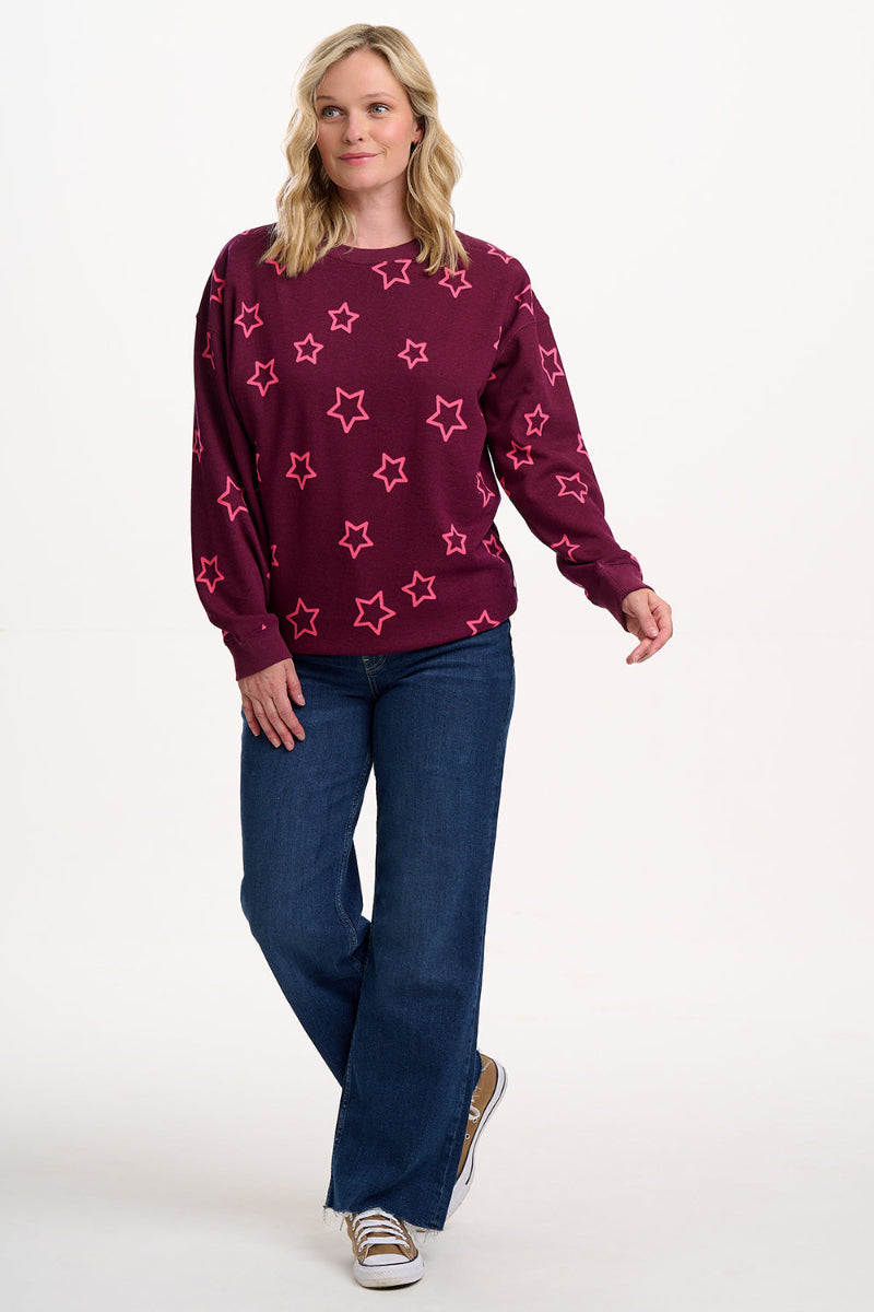 Woman wearing a maroon sweater with pink star patterns and blue jeans on a white background