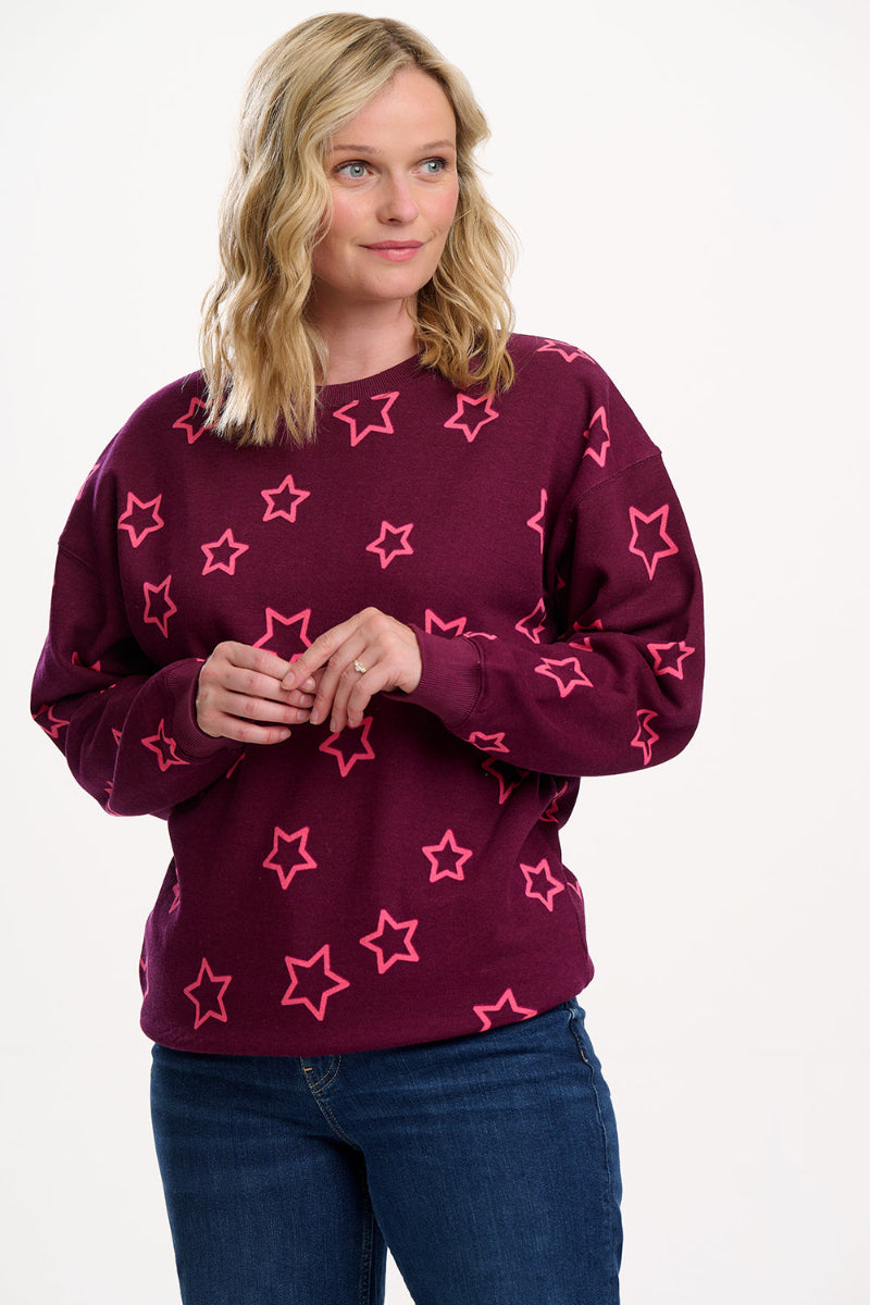 Woman wearing Sugarhill  Spaced Out Stars Sweatshirt a maroon sweater with pink star patterns on a white background