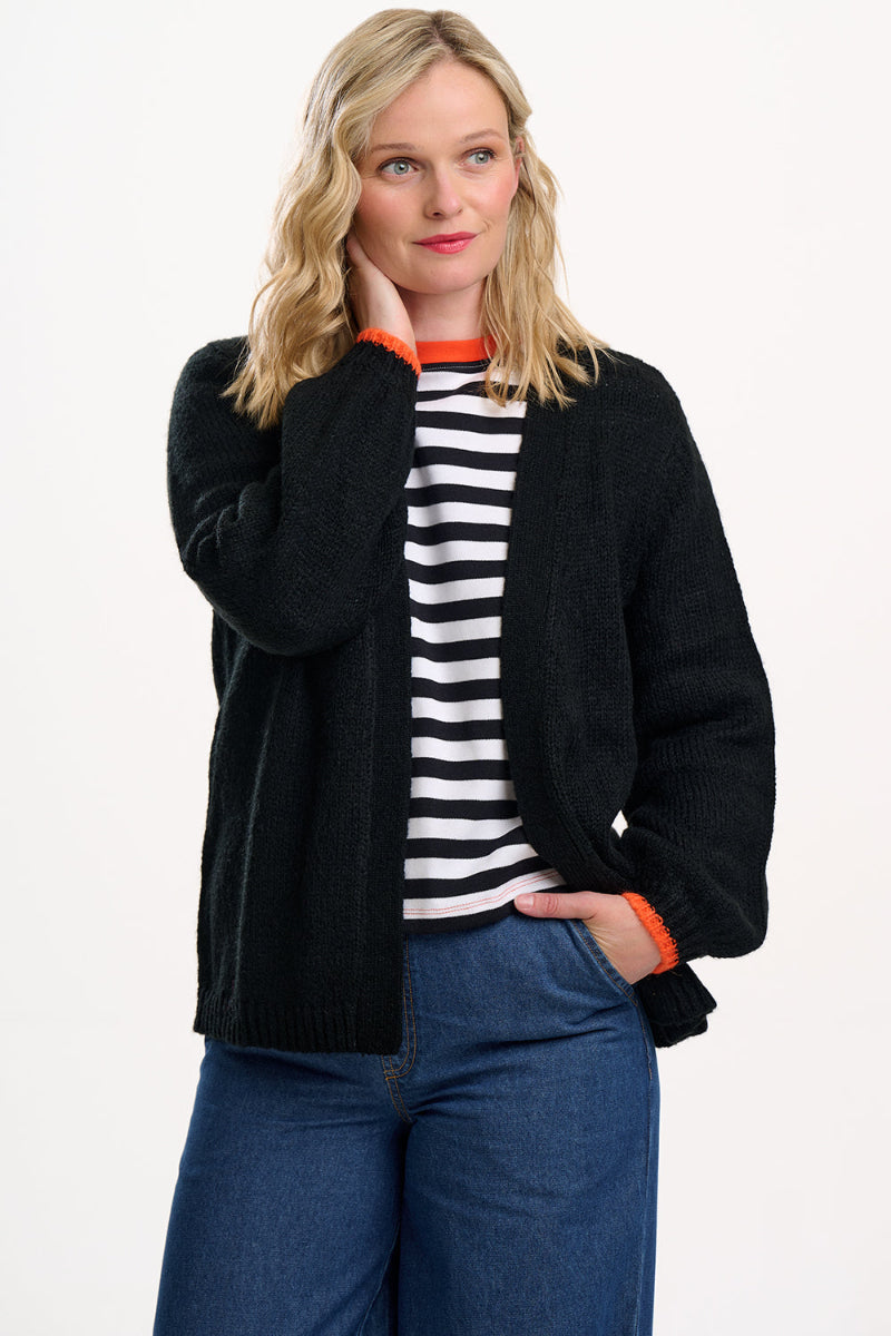 Woman wearing a Sugarhill Yvette Cardigan Black Lightning Flash over a striped shirt with blue pants on a white background