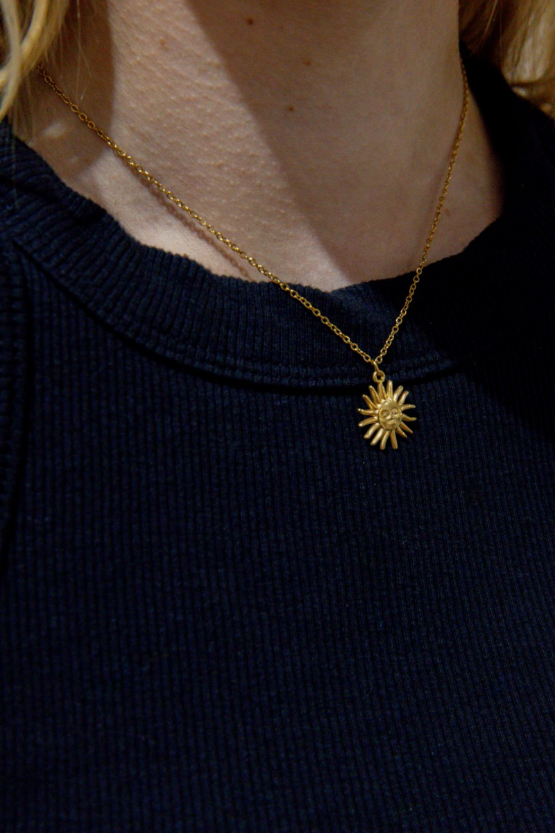 Gold necklace with a sun pendant on a person wearing a navy blue top.