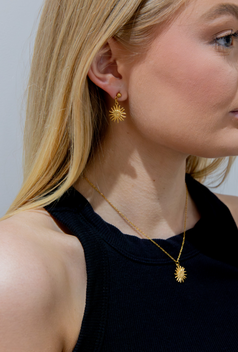 Woman wearing gold sun-shaped earrings and necklace against a neutral background