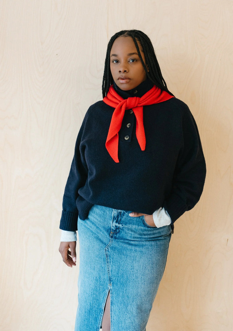 Person wearing a black sweater with a red scarf and blue jeans against a beige background