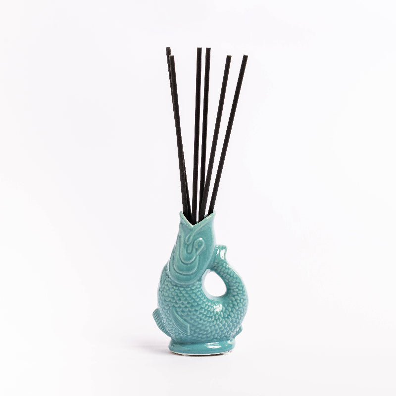 Turquoise fish-shaped diffuser with black sticks on a white background