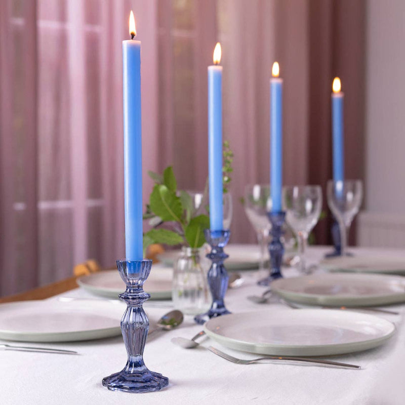 Dining table setting with blue candles in decorative holders.
