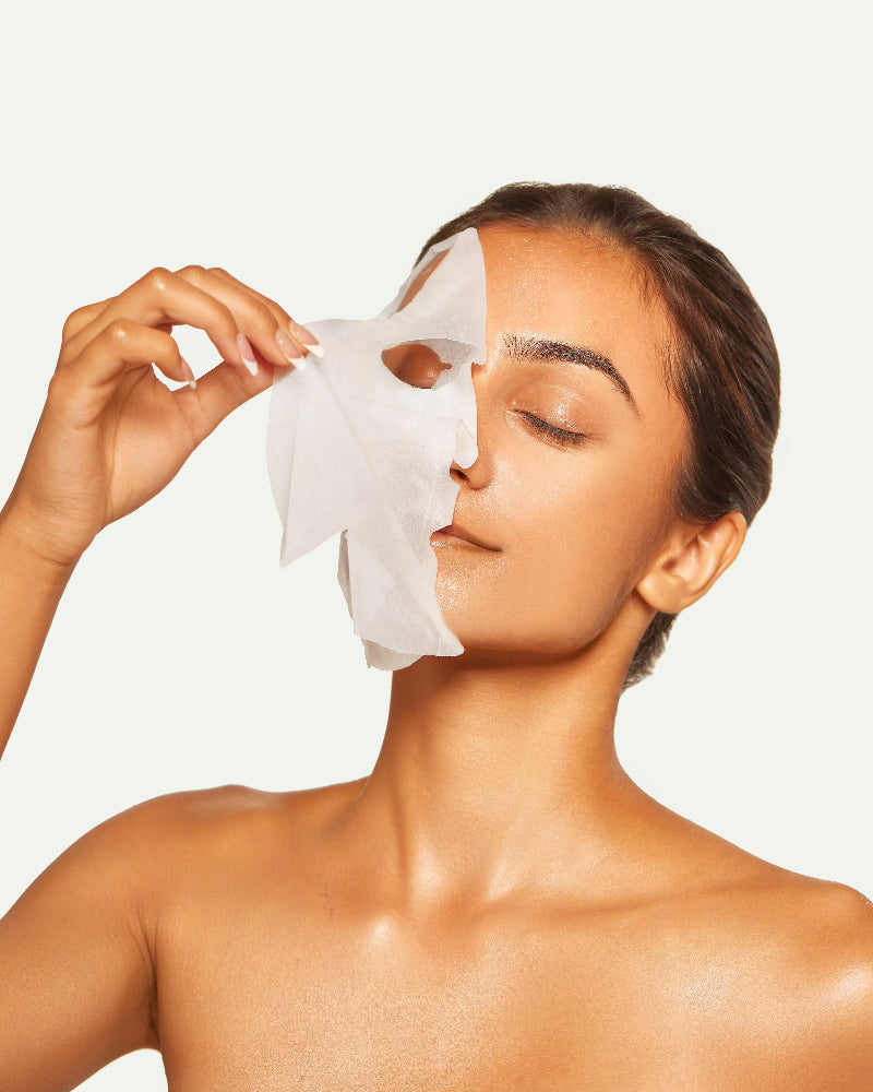 Woman applying a facial mask on a plain background