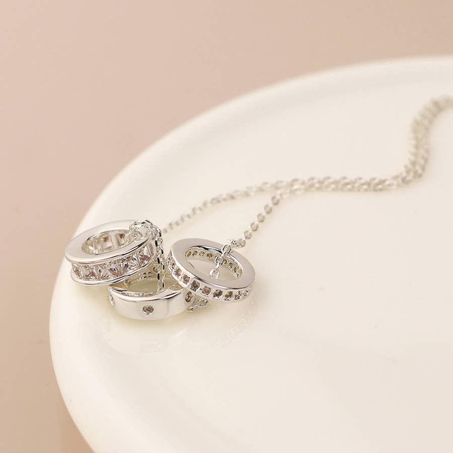 Silver hoop earrings with embedded stones on a white stand against a beige background