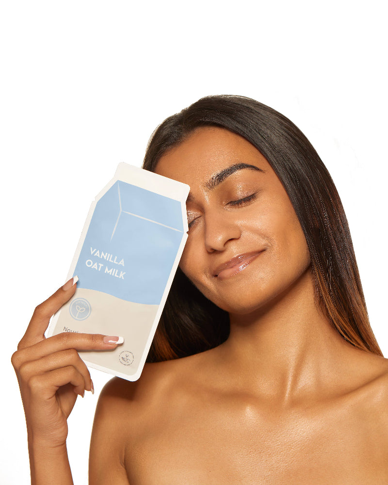 Woman holding a vanilla oat milk package against her face on a white background