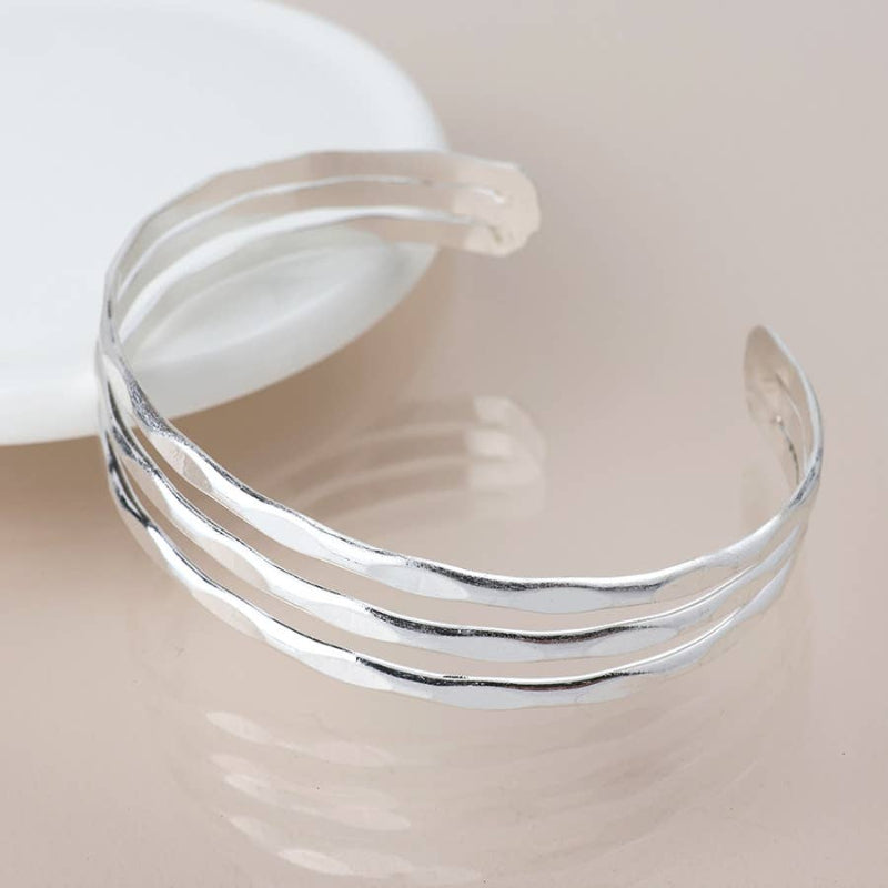 Silver bracelet with three stacked bands on a beige background