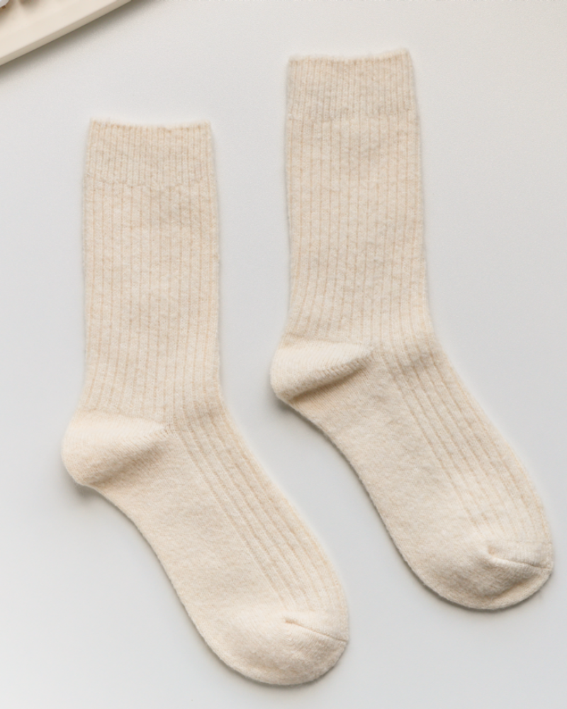 Pair of beige socks on a light gray surface with a keyboard in the background