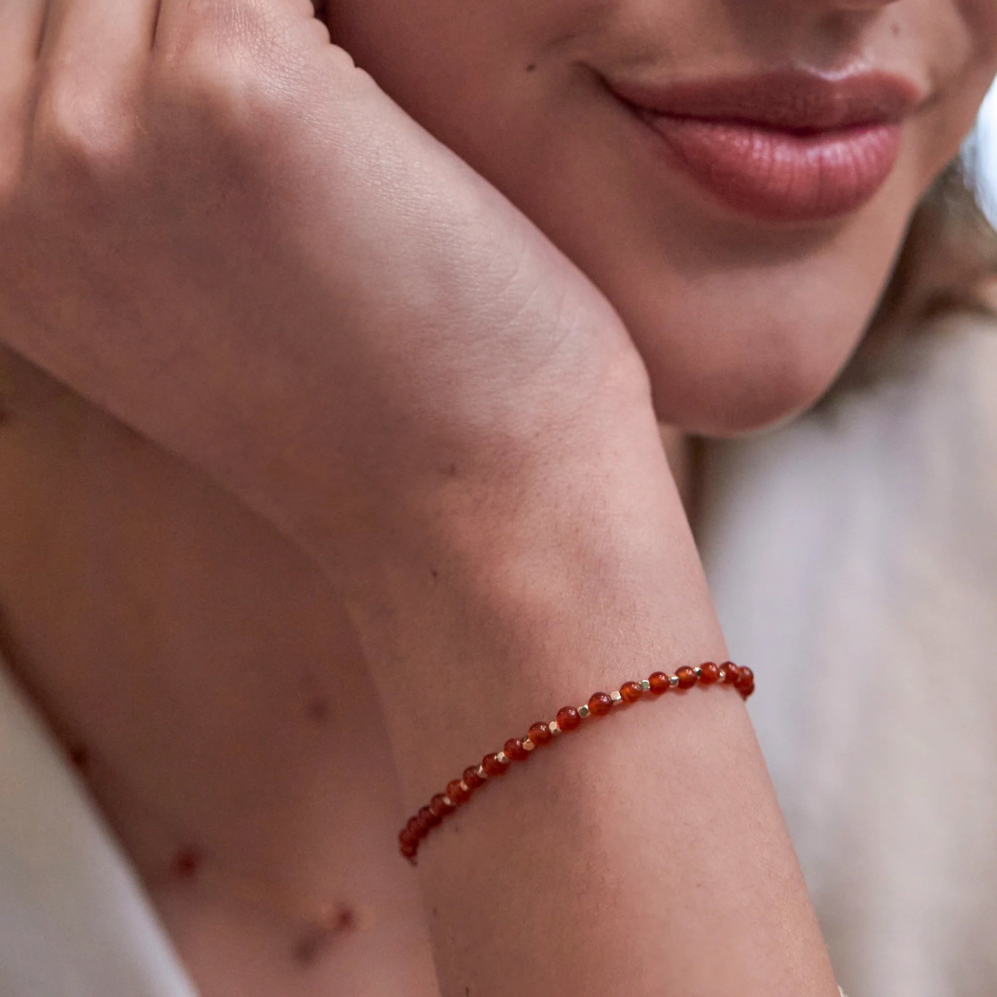 Close-up of a person wearing a red beaded bracelet on a blurred background