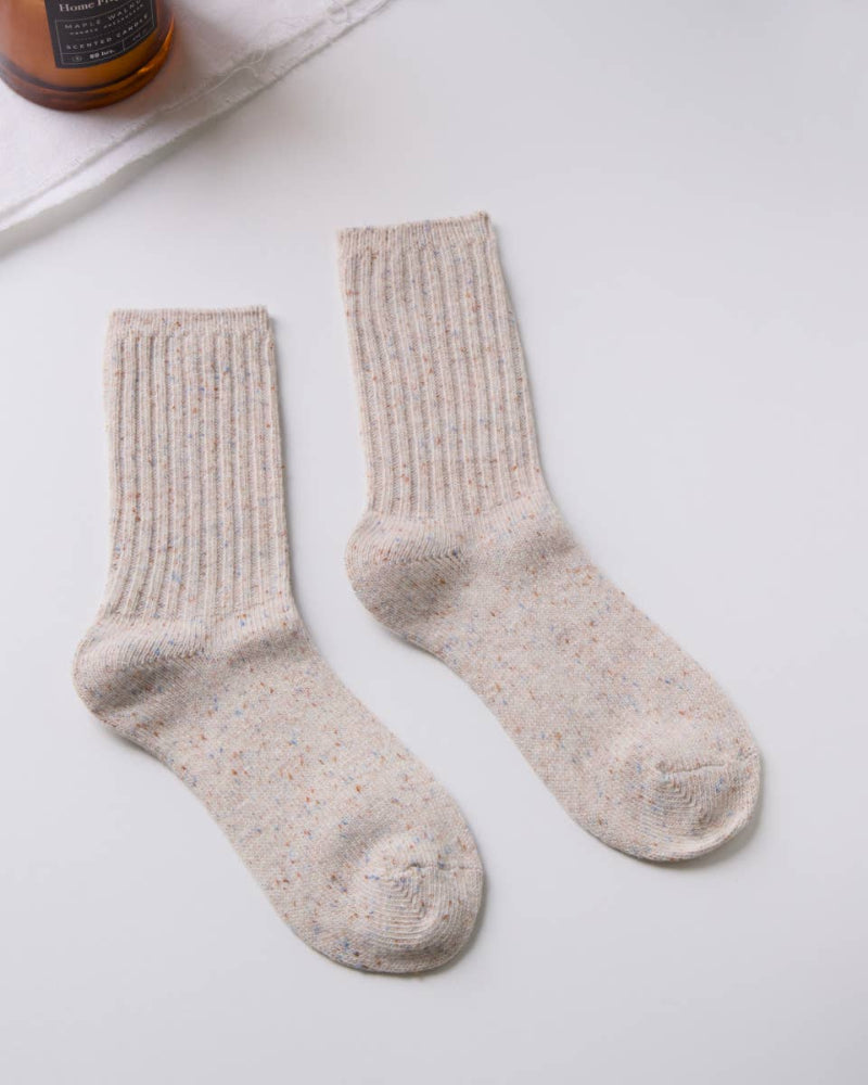 Pair of beige socks on a white surface with a bottle and white container in the background.
