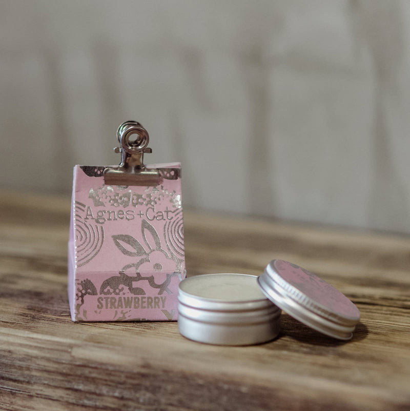 Small pink box with a silver clip and two metal tins on a wooden surface.