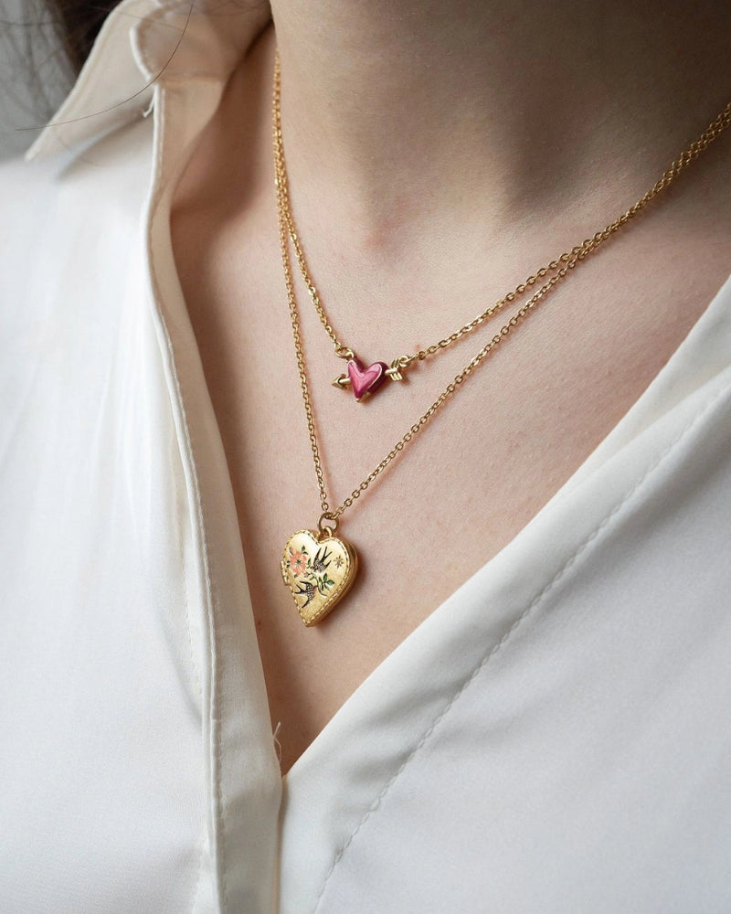Two Fable England gold necklaces with heart and pink heart pendants on a white shirt background