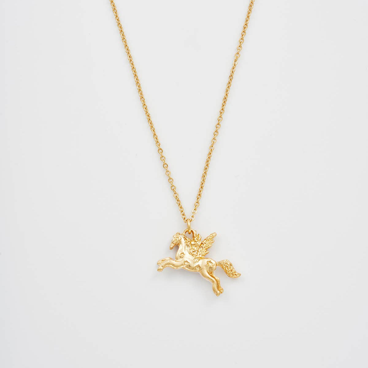 A delicate gold chain necklace featuring a small winged horse pendant, displayed against a clean, light gray background.