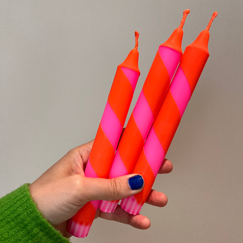 Hand holding three striped candles with pink and red pattern against a plain background