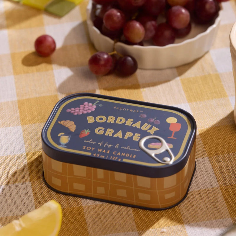 Bordeaux Grape candle tin on a checkered tablecloth with grapes and lemon slices.