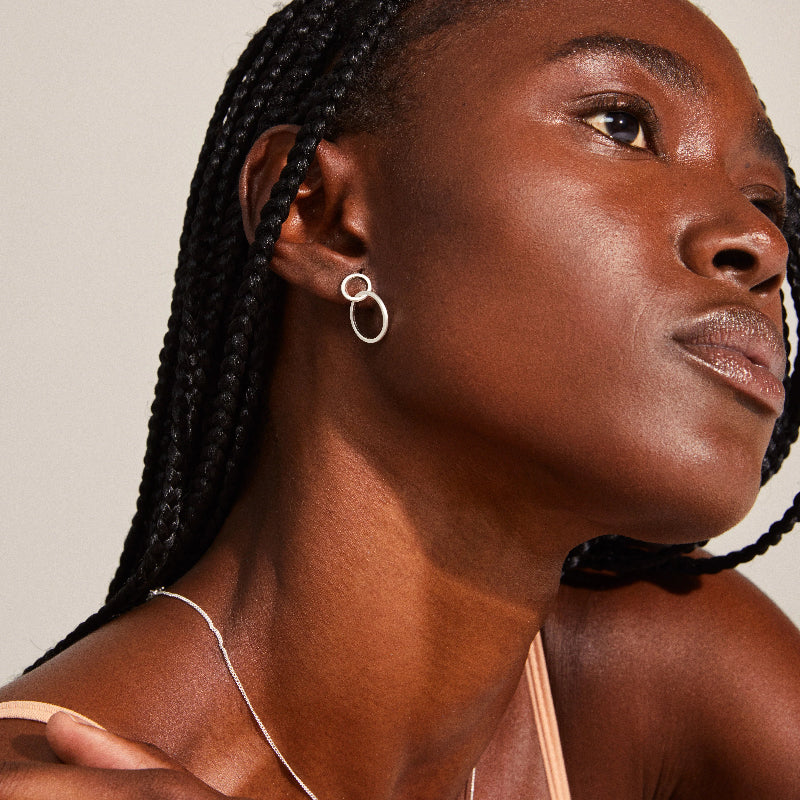 Close-up of a woman with braided hair wearing a Pilgrim Harper Earrings Silver-plated  against a neutral background