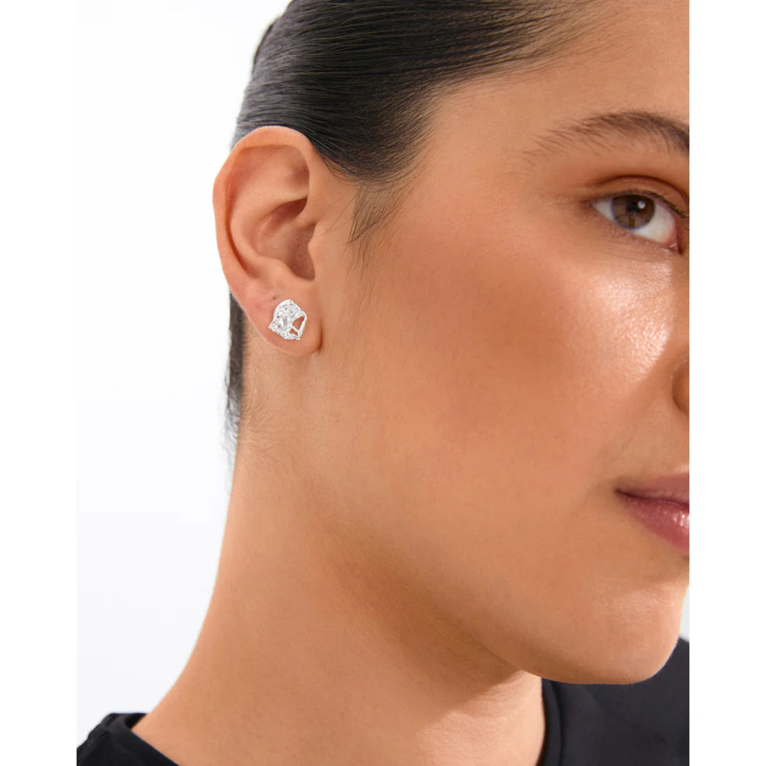 Close-up of a woman wearing a silver earring with a clear gemstone on a white background