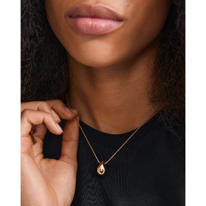 Person wearing a gold necklace with a teardrop pendant