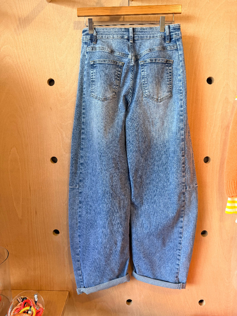 Blue jeans hanging on a wooden hanger against a wooden panel background