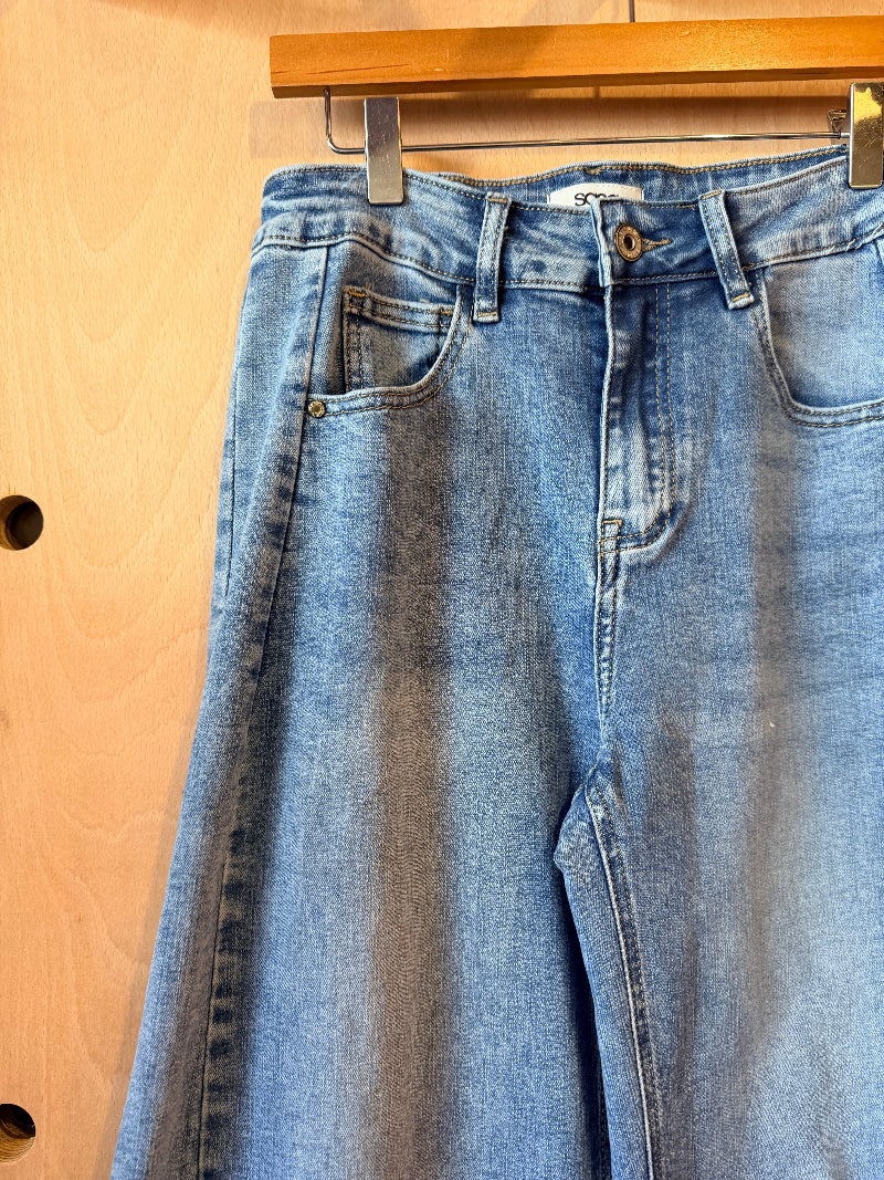 Blue jeans hanging on a wooden hanger against a wooden background