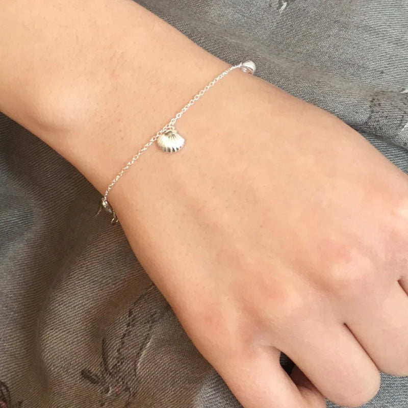 Silver bracelet with a heart charm on a wrist against a gray fabric background