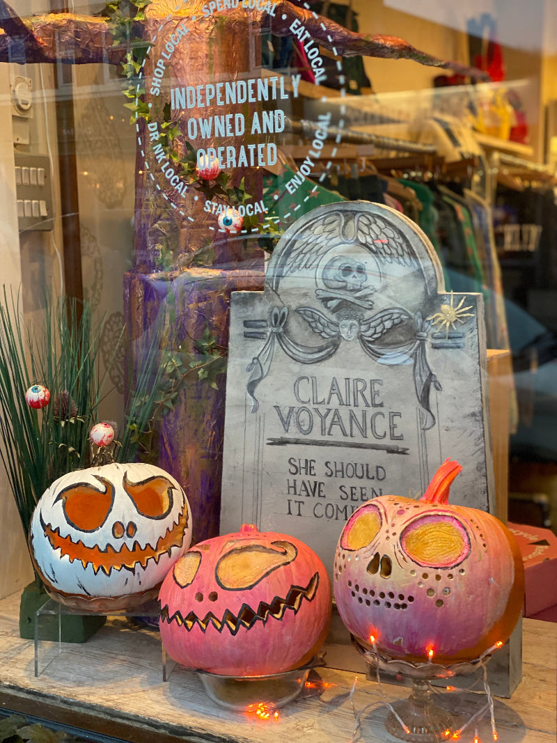Decorative pumpkins and a gravestone with text in a store window display.