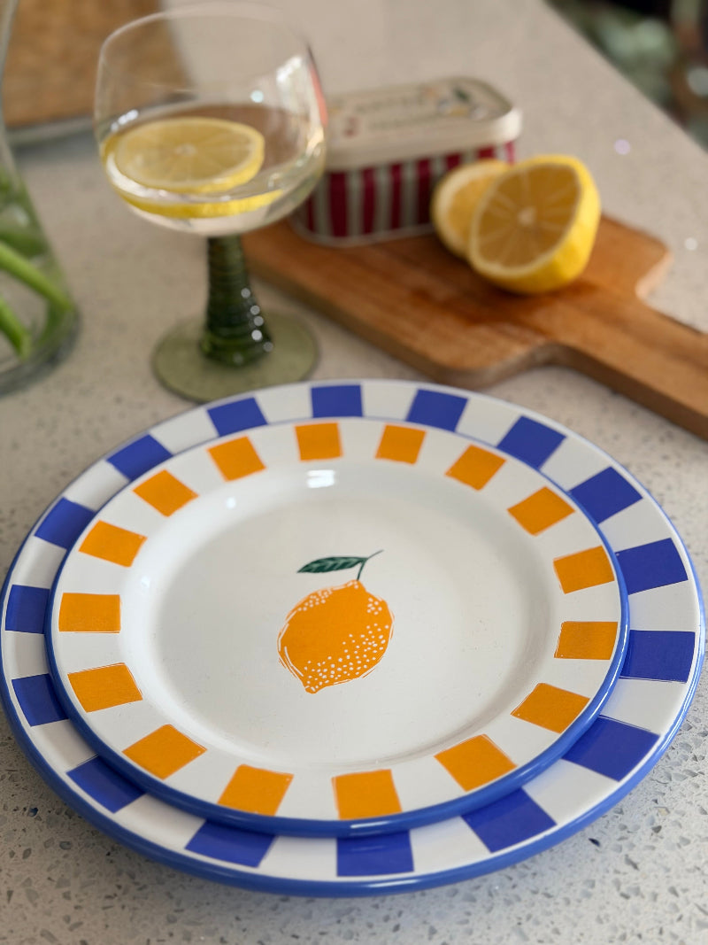 Decorative plate with orange design on a countertop with a glass of lemonade and cutting board.