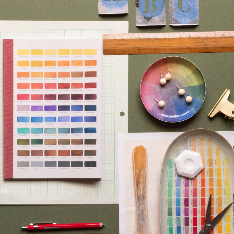 Color swatch book, paint palette, and art supplies on a green surface